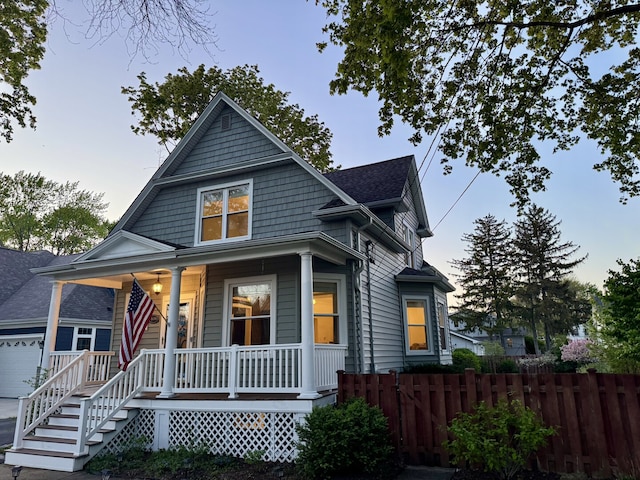 view of front of house featuring covered porch, fence, and a garage