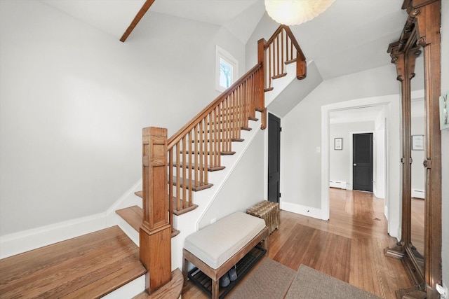 staircase with a baseboard radiator, wood finished floors, and baseboards