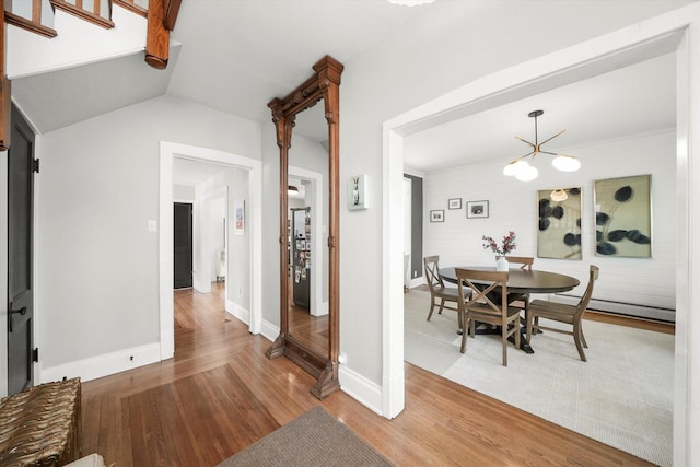 dining space featuring wood finished floors, a chandelier, a baseboard radiator, baseboards, and vaulted ceiling