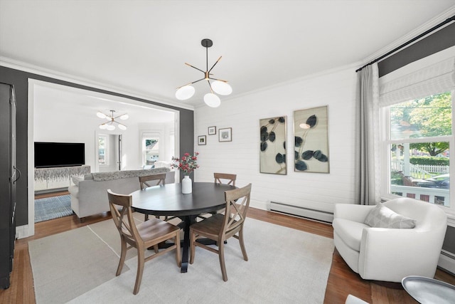 dining room featuring a chandelier, a baseboard radiator, ornamental molding, healthy amount of natural light, and wood finished floors