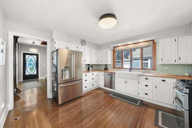 kitchen with appliances with stainless steel finishes, backsplash, white cabinetry, a sink, and dark wood-type flooring