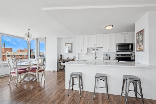 kitchen featuring appliances with stainless steel finishes, a chandelier, a sink, a kitchen bar, and white cabinets