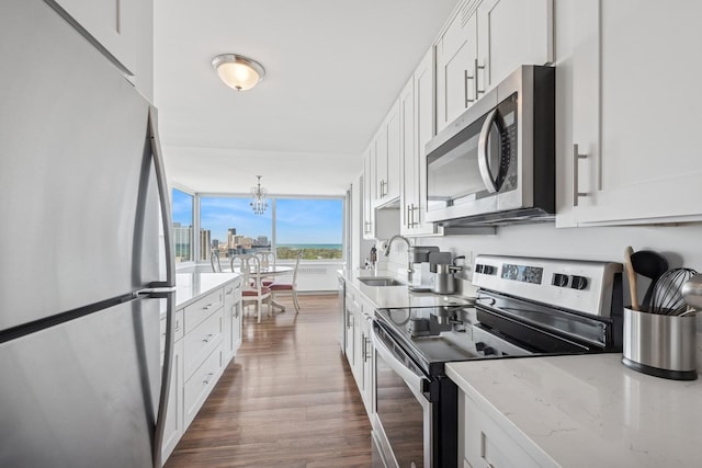 kitchen with stainless steel appliances, a sink, white cabinets, dark wood-style floors, and light stone counters