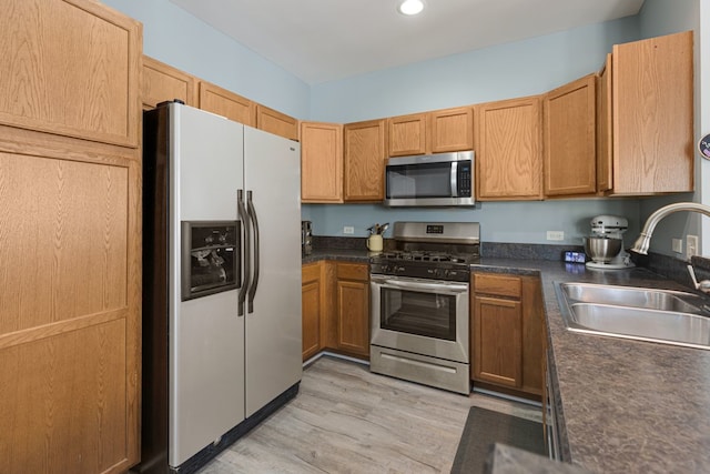 kitchen featuring stainless steel appliances, a sink, dark countertops, light wood-type flooring, and recessed lighting
