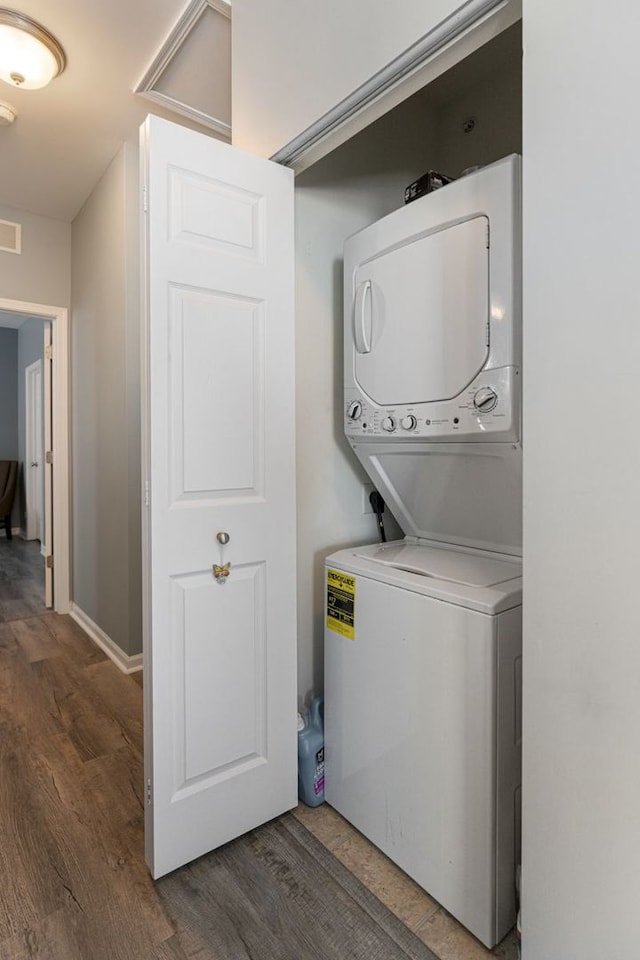 laundry area featuring stacked washer and clothes dryer, wood finished floors, and baseboards