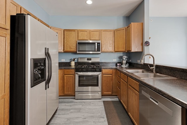 kitchen featuring stainless steel appliances, a sink, dark countertops, light wood-style floors, and recessed lighting