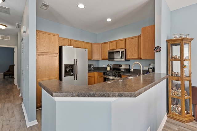kitchen with appliances with stainless steel finishes, dark countertops, a sink, light wood-style flooring, and recessed lighting