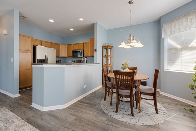 kitchen featuring fridge with ice dispenser, stainless steel microwave, a chandelier, baseboards, and wood finished floors