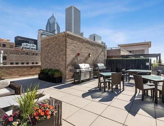 view of patio with outdoor dining space, area for grilling, fence, and a view of city