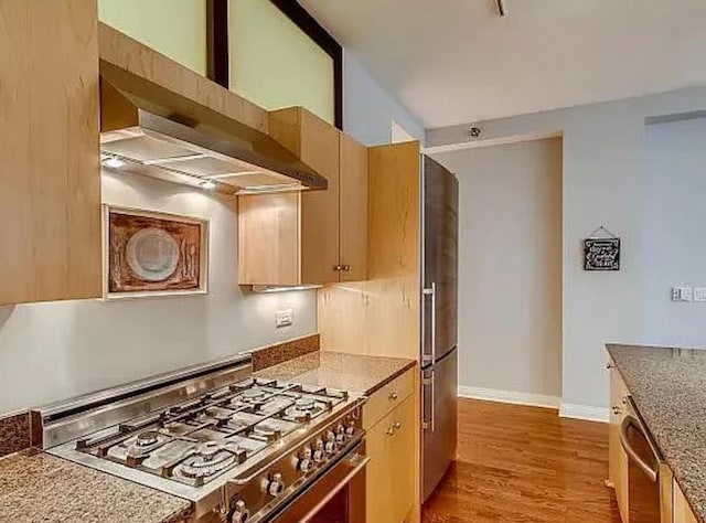 kitchen with stainless steel appliances, wall chimney exhaust hood, light wood-style flooring, baseboards, and light stone countertops