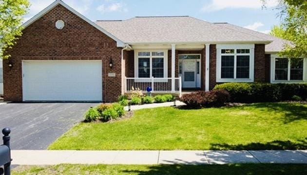 single story home with covered porch, asphalt driveway, a front yard, brick siding, and an attached garage