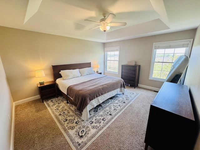 bedroom featuring a raised ceiling, light colored carpet, baseboards, and a ceiling fan