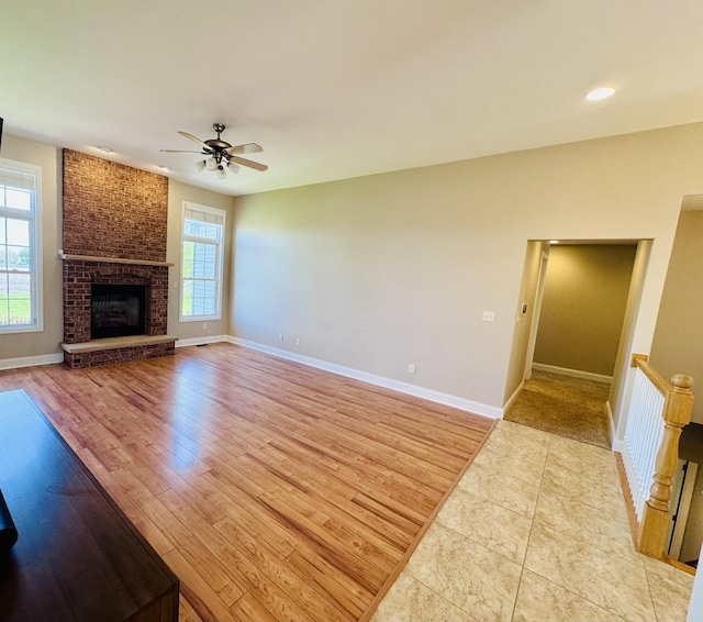unfurnished living room with a ceiling fan, baseboards, light wood-type flooring, and a brick fireplace