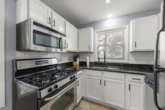 kitchen with appliances with stainless steel finishes, a sink, white cabinetry, backsplash, and dark stone counters