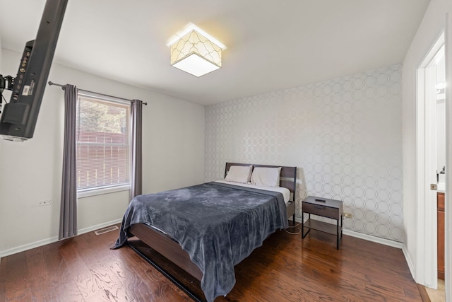 bedroom featuring wallpapered walls, an accent wall, baseboards, and wood finished floors