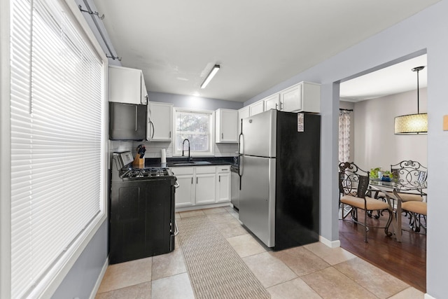 kitchen with appliances with stainless steel finishes, dark countertops, a sink, white cabinets, and baseboards