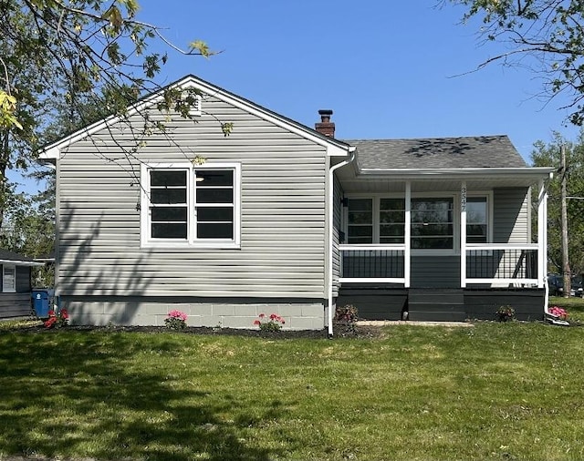 rear view of house with a lawn, a chimney, covered porch, and a shingled roof