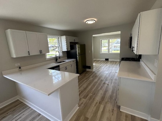 kitchen with freestanding refrigerator, light wood-type flooring, light countertops, and a sink