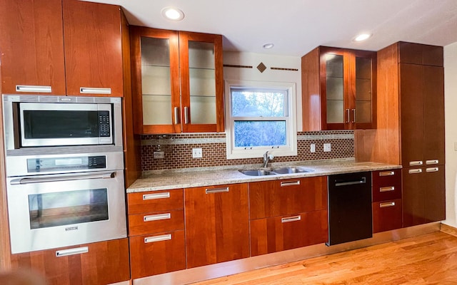 kitchen featuring appliances with stainless steel finishes, a sink, light stone countertops, decorative backsplash, and glass insert cabinets