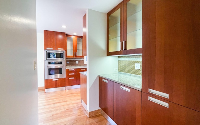 kitchen featuring stainless steel appliances, decorative backsplash, light wood-style flooring, glass insert cabinets, and light stone countertops