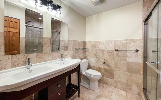 bathroom with tile walls, a shower stall, toilet, double vanity, and a wainscoted wall