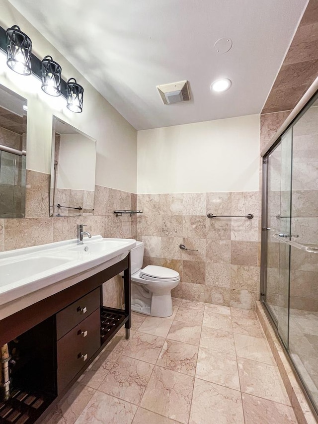 bathroom featuring tile walls, a shower stall, toilet, double vanity, and a wainscoted wall