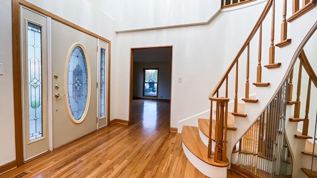 foyer with light wood-style flooring, stairway, baseboards, and a high ceiling