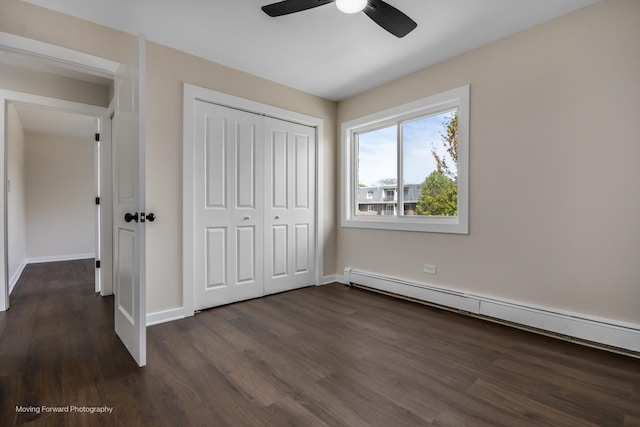 unfurnished bedroom with a baseboard radiator, dark wood finished floors, a closet, baseboards, and a ceiling fan