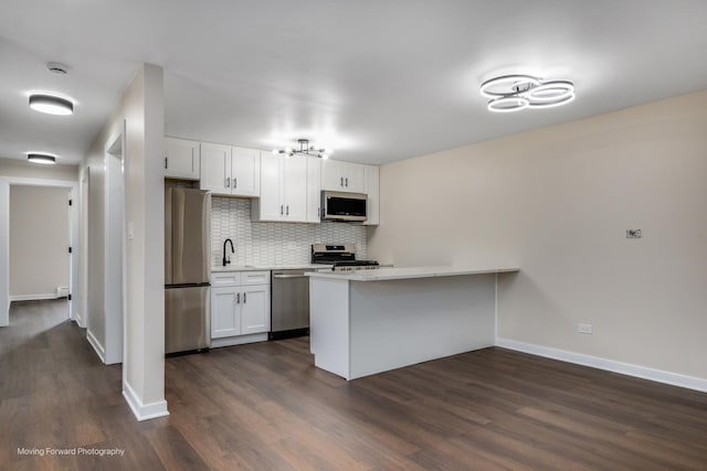 kitchen featuring stainless steel appliances, a sink, backsplash, a peninsula, and dark wood finished floors