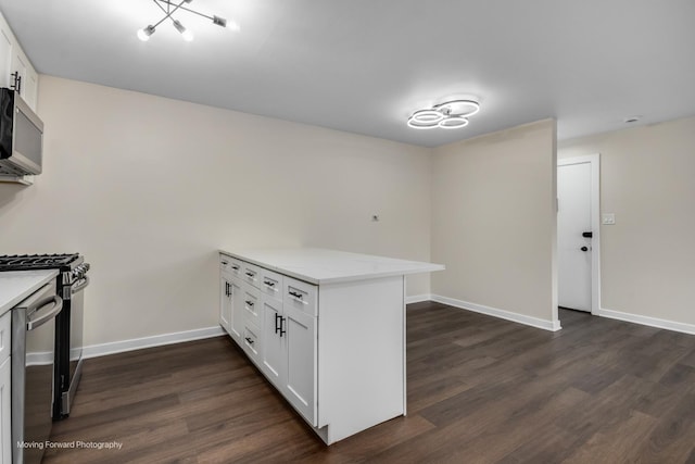 kitchen with stainless steel microwave, a peninsula, gas range oven, white cabinets, and dark wood finished floors