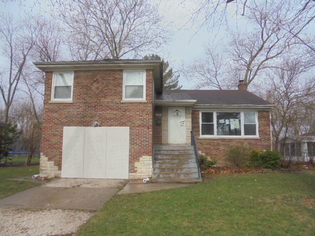 tri-level home with brick siding, a front lawn, a chimney, and driveway