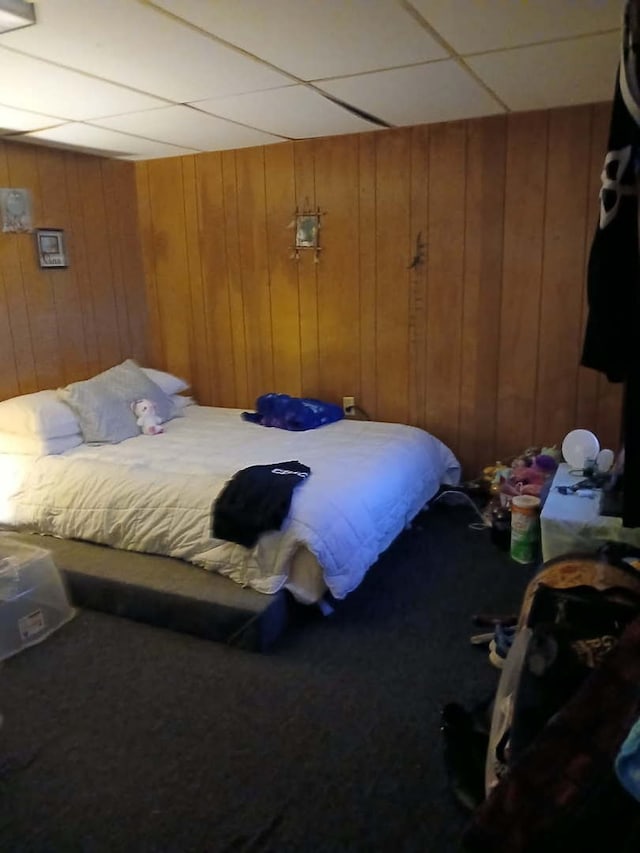 bedroom featuring a paneled ceiling, wooden walls, and carpet floors