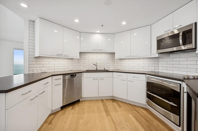 kitchen with stainless steel appliances, a sink, white cabinetry, dark countertops, and light wood-type flooring