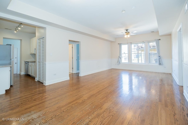 unfurnished living room with a ceiling fan, wood finished floors, track lighting, and a wainscoted wall