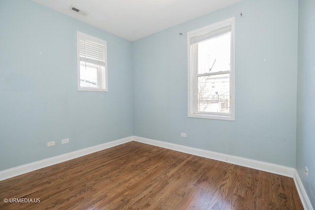 spare room featuring healthy amount of natural light, baseboards, and dark wood finished floors