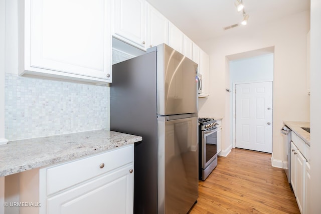 kitchen featuring stainless steel appliances, white cabinets, tasteful backsplash, light wood-style flooring, and light stone counters