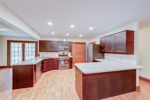 kitchen with appliances with stainless steel finishes, a peninsula, a sink, light wood-style floors, and light countertops