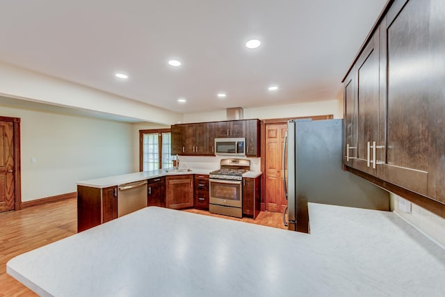 kitchen with appliances with stainless steel finishes, a peninsula, recessed lighting, baseboards, and light wood finished floors