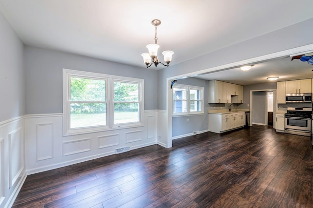 kitchen with stainless steel appliances, light countertops, a chandelier, a wainscoted wall, and a sink