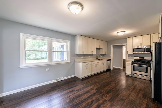 kitchen featuring stainless steel appliances, dark wood-style flooring, a sink, baseboards, and white cabinetry