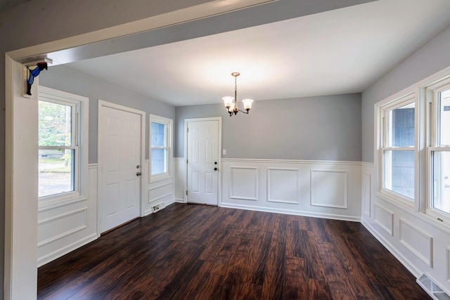 unfurnished dining area with a chandelier, dark wood finished floors, wainscoting, and a decorative wall
