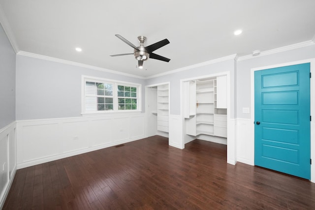unfurnished bedroom with a decorative wall, wood-type flooring, ornamental molding, a ceiling fan, and two closets