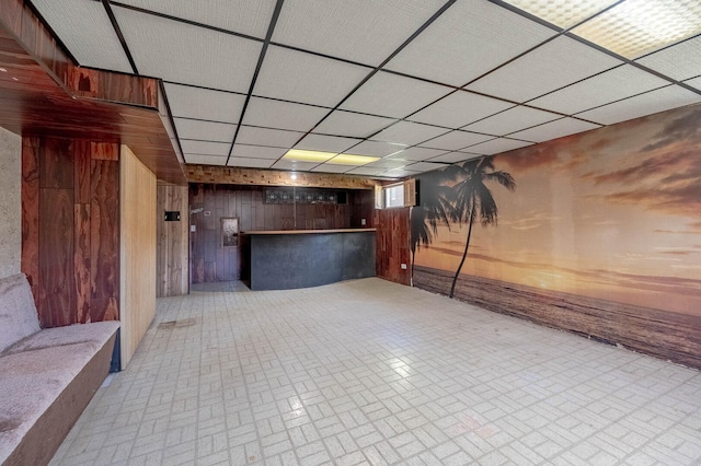 basement featuring wood walls, brick patterned floors, and a paneled ceiling