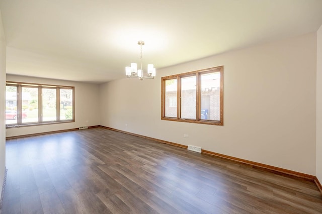 unfurnished room with a chandelier, healthy amount of natural light, and dark wood-type flooring
