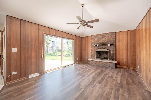 unfurnished living room with ceiling fan, wood finished floors, a brick fireplace, wooden walls, and vaulted ceiling