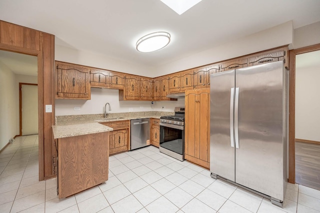 kitchen featuring appliances with stainless steel finishes, a sink, brown cabinetry, under cabinet range hood, and light tile patterned floors