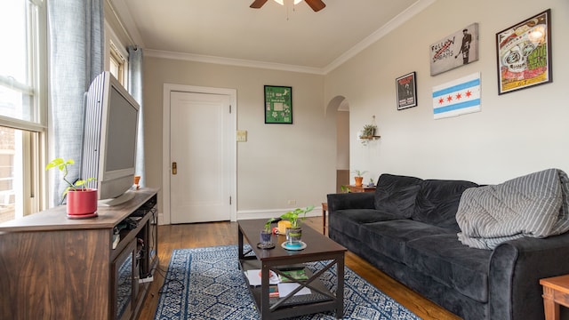 living room featuring arched walkways, a ceiling fan, wood finished floors, ornamental molding, and baseboards