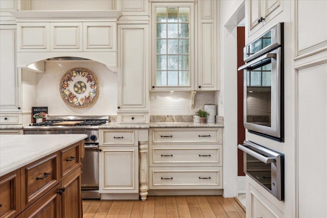 2423 Harrison St, Evanston, IL 60201 - kitchen featuring appliances with stainless steel finishes, backsplash, light stone countertops, light wood-style flooring, and cream cabinets