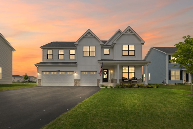 view of front of home with covered porch, an attached garage, driveway, a front yard, and stone siding