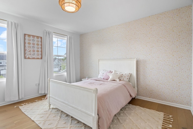 bedroom with wallpapered walls, wood finished floors, and baseboards